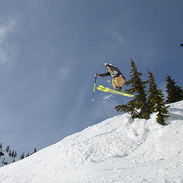 man skiing off of big jump getting air blue bird day
