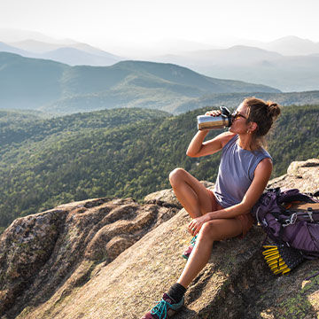 woman sitting on rock drinking from a water bottle