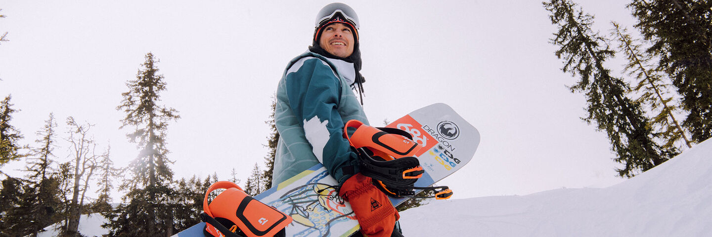 Snowboarder surveys a winter landscape while holding his board