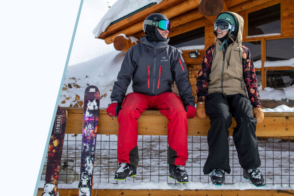two skiers sitting on a railing and chatting