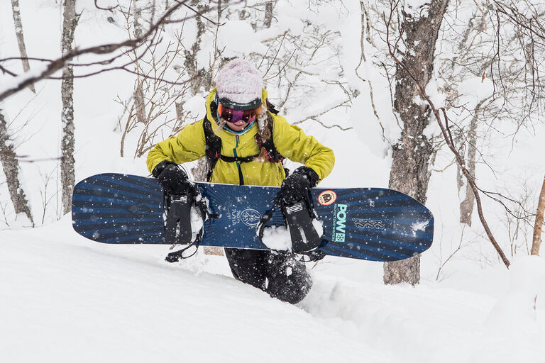 woman carrying snowboard in powder